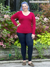 Woman standing in front of plants wearing Miik's Lisa2 high waisted legging in navy in long length with a red top.