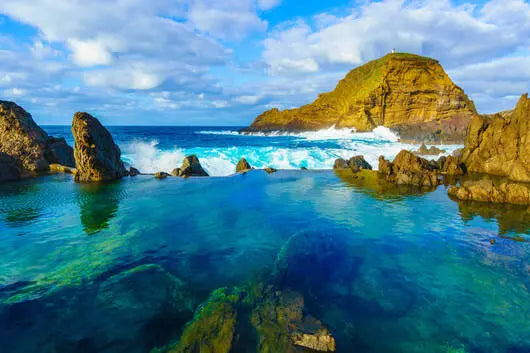 Rocks and clear blue water with a partly cloudy sky