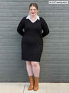 Woman standing in front of a brick wall wearing Miik's Adelaide collared faux layered dress in black and brown boots