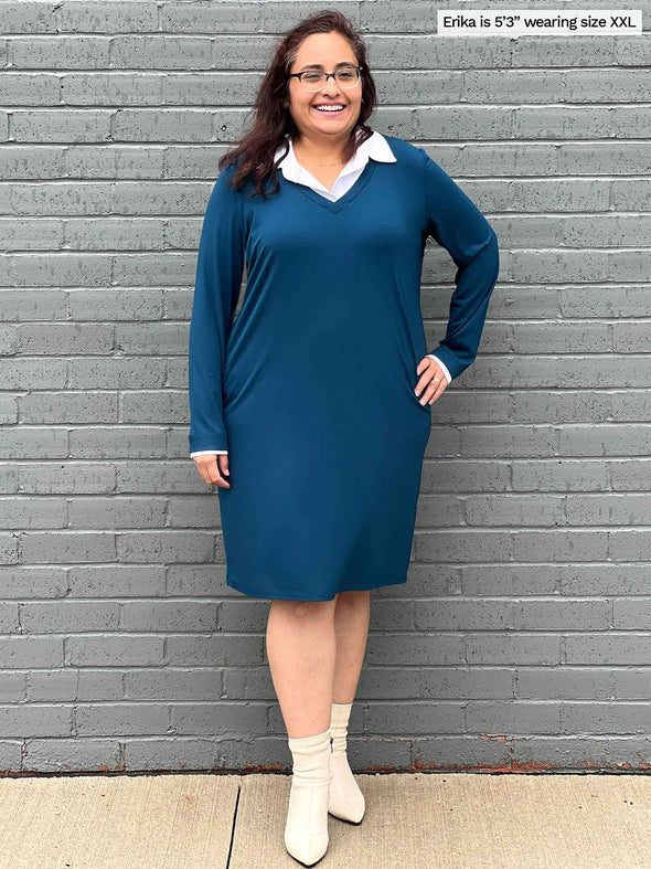 Woman smiling standing in front of a brick wall wearing Miik's Adelaide collared faux layered dress in teal