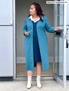 Woman looking away while opening a door wearing Miik's Adelaide collared faux layered dress in teal with a long cardigan in teal melange 