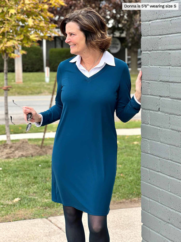 Woman smiling and looking away next to a brick wall wearing Miik's Adelaide collared faux layered dress in teal