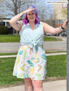 Woman standing in nature wearing Miik's Astrid spaghetti strap dress in green leaf pattern with a button up top over it.