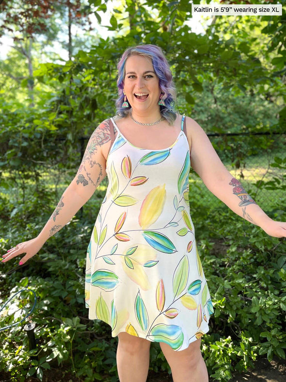 Woman standing in nature wearing Miik's Astrid spaghetti strap dress in green leaf pattern.