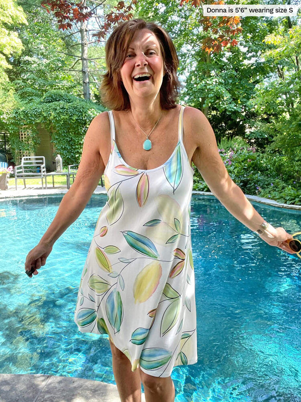 Woman standing in front of a pool wearing Miik's Astrid spaghetti strap dress in green leaf pattern.