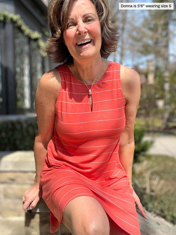 Miik founder Donna (five feet six, size small) sitting in a backyard smiling wearing Miik's Aubrey reversible swing dress in papaya wide pinstripe