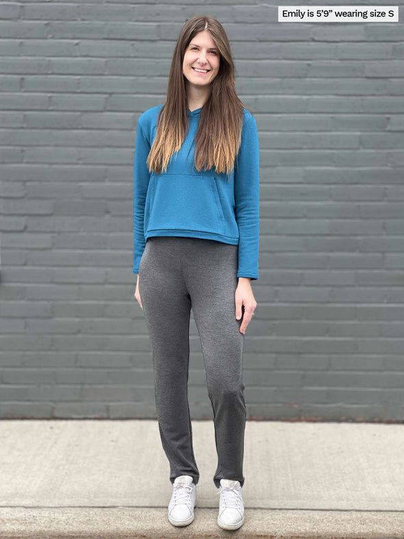 Woman smiling standing in front of a brick wall wearing Miik's Avery pull-on pant in granite melange french terry along with a teal melange cropped hoodie and white shoes