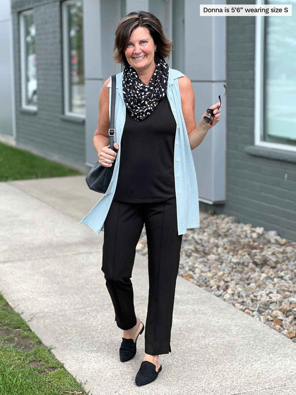 Woman standing in front of a building wearing Miik's Avy button-up dressy tunic top in blue as a cardigan with an all black outfit underneath.