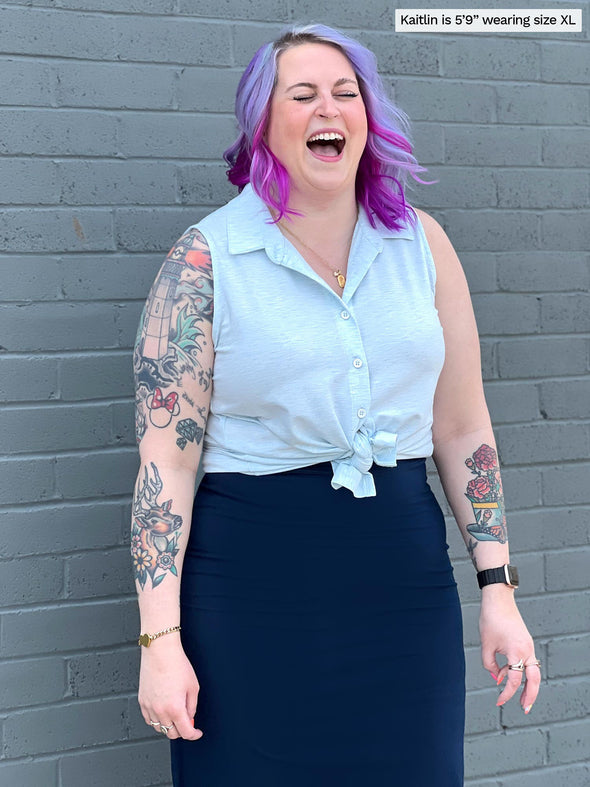 Woman standing in front of a brick wall laughing while wearing Miik's Avy button-up dressy tunic top tied in waterfall melange whit a navy long skirt.
