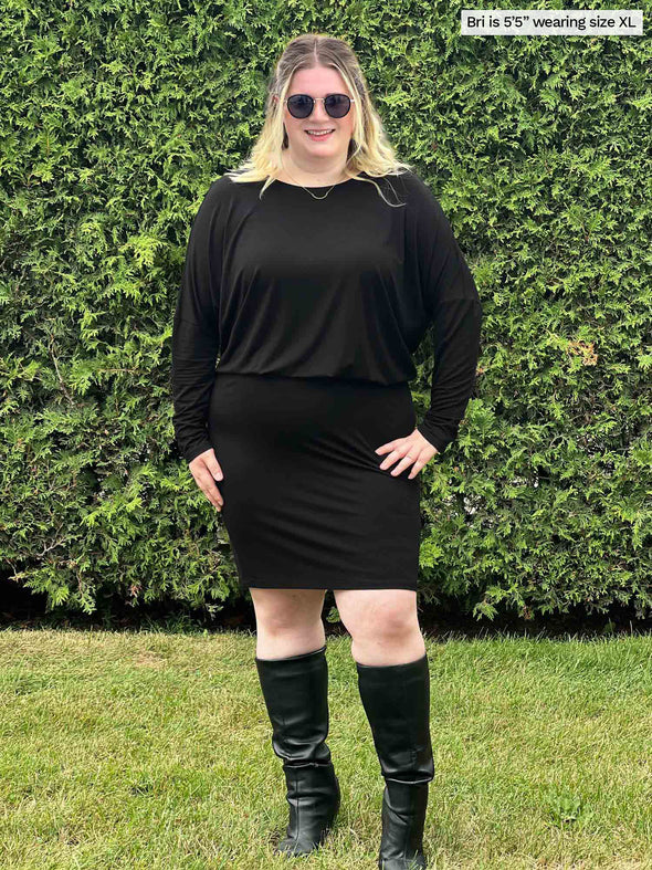 Woman standing in nature wearing Bali bat sleeve dress in black with matching colour boots and sunglasses