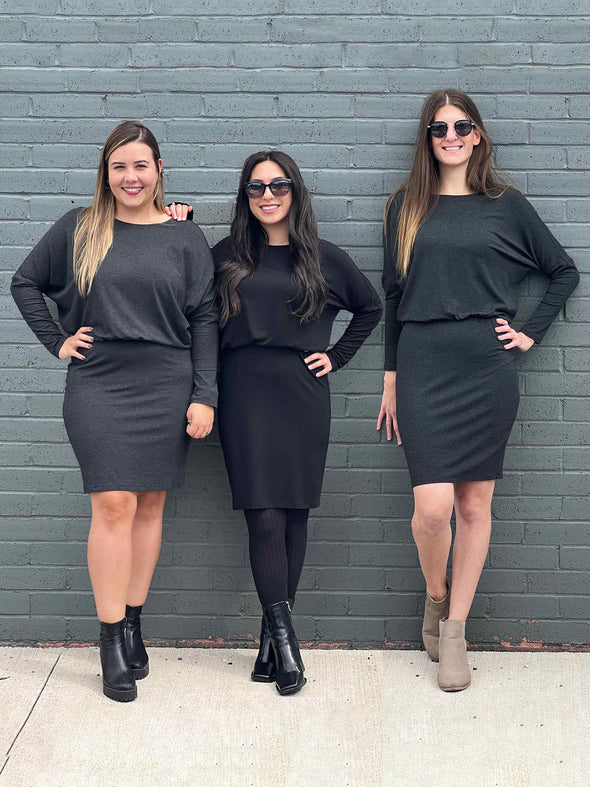 Three women standing in front of a brick wall wearing Miik's Bali bat sleeve dress in charcoal and black