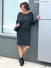 Woman looking away standing in front of a window wearing Miik's Bali bat sleeve dress in charcoal