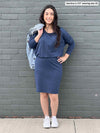 Woman standing in front of a wall wearing Miik's Bali batwing sleeve dress in navy melange with a jean jacket thrown over her shoulder.
