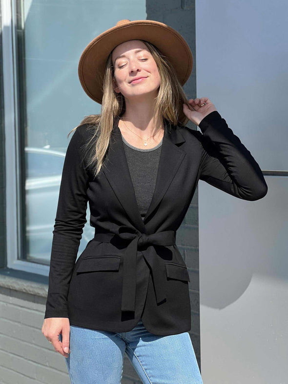 Woman standing in front of a building wearing Miik's Blair bamboo tie waist belt with a black blazer and jeans.