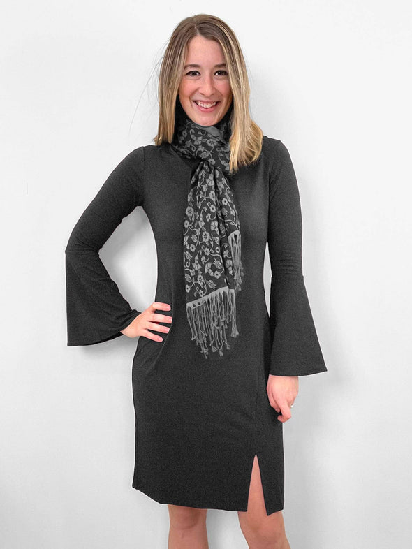 Woman standing in front of a wall wearing Miik's Brianne bell sleeve dress in grey with a scarf.