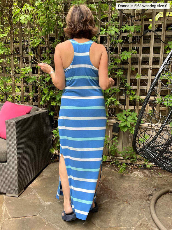 Woman standing in front of trellis with her back showing to the camera while wearing Miik's brodie racerback tank maxi dress in blue stripe color