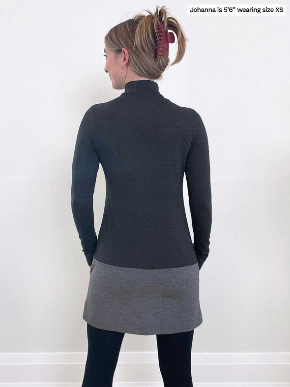 Woman standing in front of a wall wearing Miik's Brooklin mock neck pocket tunic in charcoal grey.