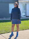 Woman standing on a sidewalk wearing Miik's Brooklin mock neck pocket tunic in navy/navy melange as a dress with her hand in one pocket.