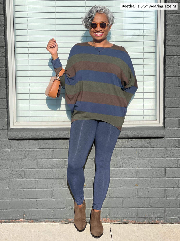 Woman standing in front of a window wearing Miik's Cami dolman top in brown green blue with navy leggings.