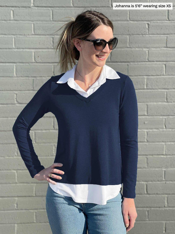 Woman standing in front of a brick wall wearing Miik's Carson collared faux-layer shirt in navy with jeans and sunglasses 