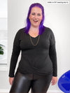 Woman standing in front of a wall wearing Miik's Chenley twist-front top in grey with leather leggings.