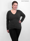 Woman standing in front of a wall wearing Miik's Chenley twist-front top in grey with black leggings.