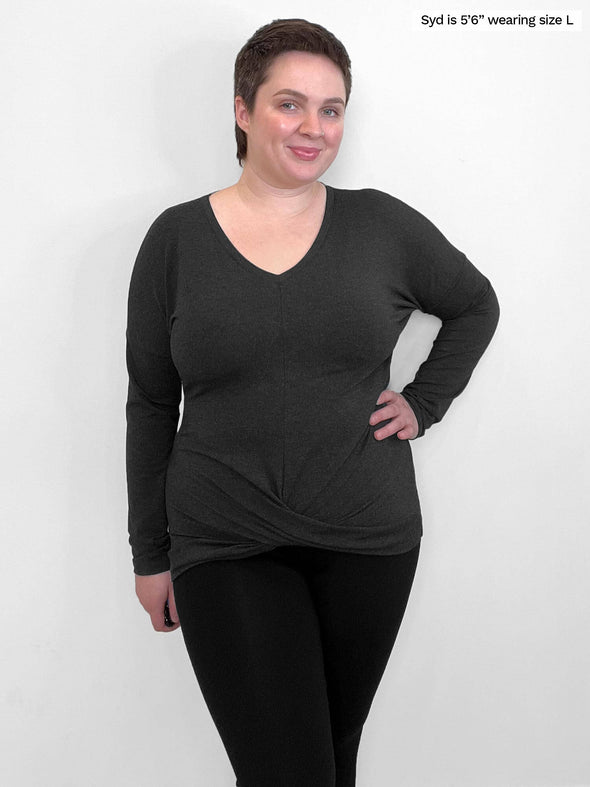 Woman standing in front of a wall wearing Miik's Chenley twist-front top in grey with black leggings.