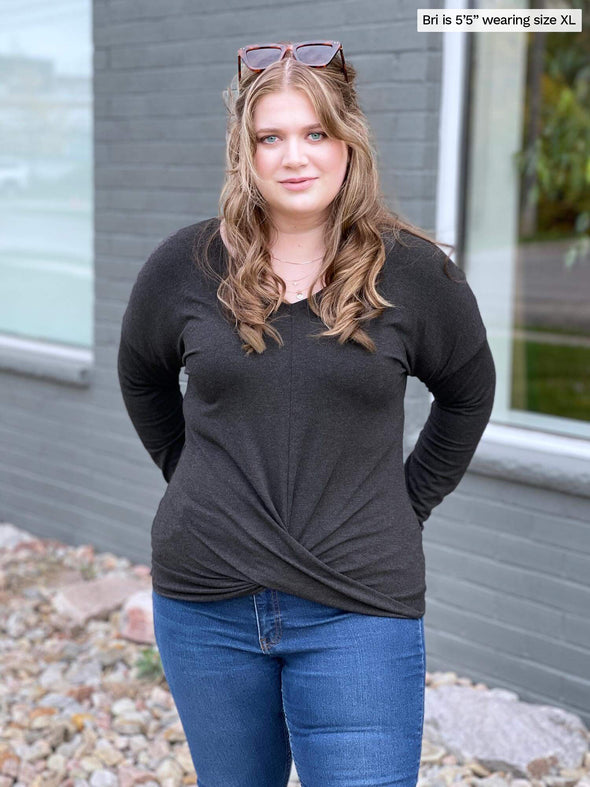 Woman standing in front of a building wearing Miik's Chenley twist-front top in grey with jeans.