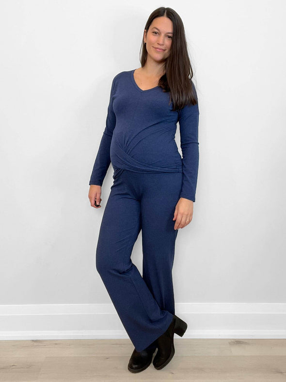 Woman standing in front of a wall wearing Miik's Chenley twist-front top in blue with matching pants.