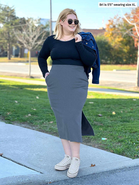 Woman smiling while looking away wearing Miik's Devon midi skirt in granite with a long sleeve top in charcoal and sneakers  