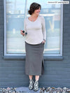 Woman smiling looking away while standing in front of a window wearing Miik's Devon midi skirt in grey granite melange with a long sleeve top in oatmeal melange