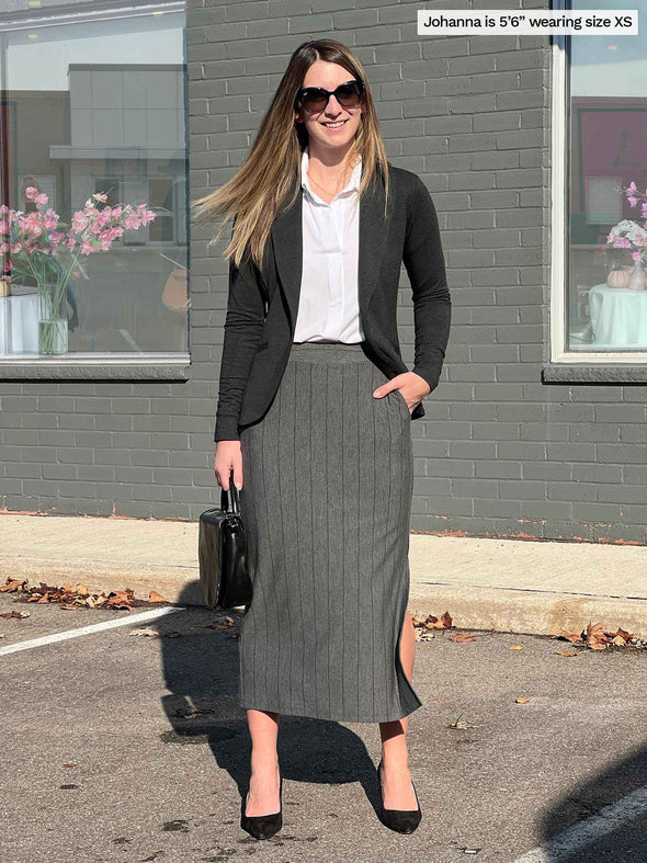 Woman smiling standing in a parking lot wearing Miik's Devon midi skirt in grey granite pinstripe with a collared white top and a charcoal blazer  