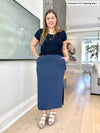 Woman smiling standing in a living room wearing Miik's Devon pocket midi skirt in navy melange with a navy solide basic tee