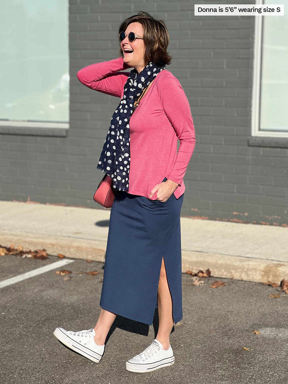 Woman smiling and standing sideway in a parking lot wearing Miik's Devon midi skirt in navy melange with a pink pomegranate long sleeve top with a blue polka dot scarf