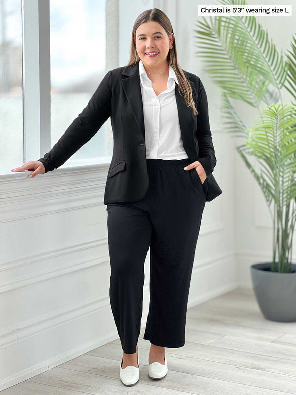 Miik model Christtal (five fee three, size large) standing next to a window wearing Miik's  Easton pocket capri in black with a open blazer in the same colour and a collared shirt in white