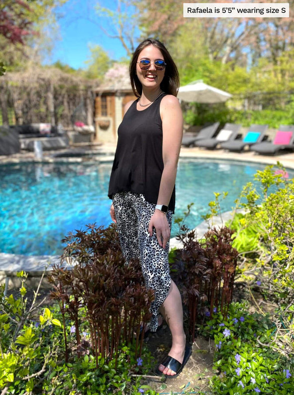 Woman standing in front of a pool smiling while wearing Eliana high-low tank top in black colour.