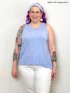 Woman standing in front of a white wall laughing while wearing Miik's Eliana high-low tank top in light blue colour.