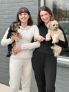 Two women smiling while both are holding puppies wearing Miik's Essex cropped fleece hoodie in oatmeal and black