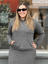 Woman smiling standing in front of a window wearing Miik's Essex cropped fleece hoodie in granite melange with a granite pinstripe skirt and sunglasses 