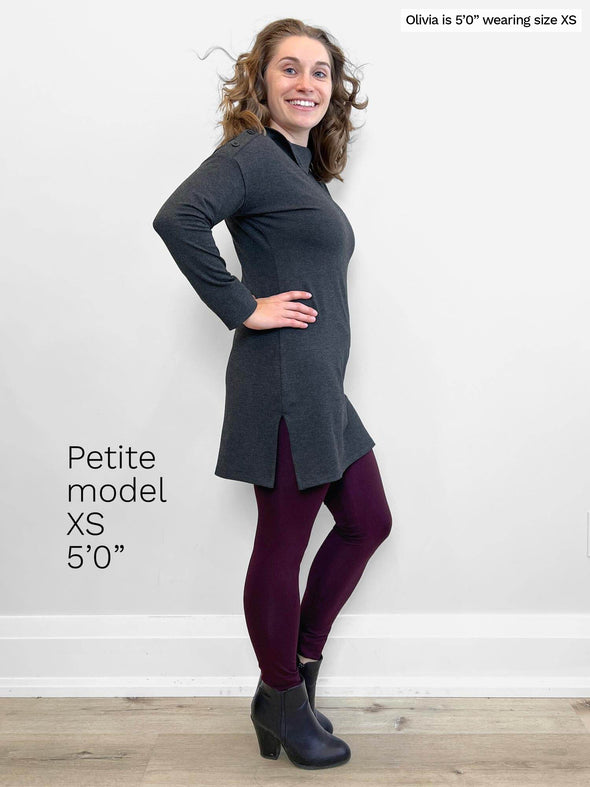 Woman standing sideway in front of a white wall wearing Miik's Fergie buttoned long sleeve tunic in charcoal with legging in port colour 