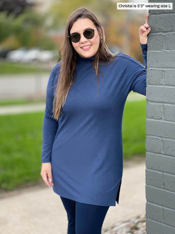 Woman standing next to a brick wall wearing Miik's Fergie buttoned long sleeve tunic in navy melange with a navy legging and sunglasses