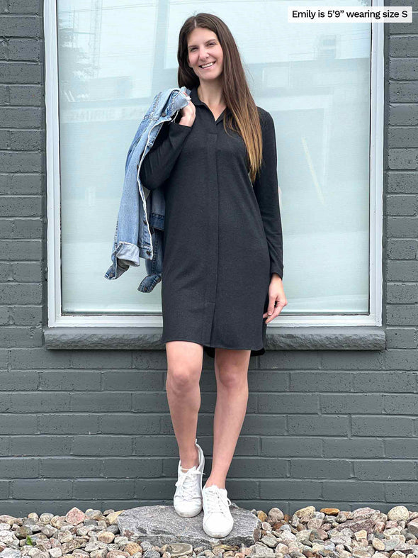 Woman standing in front of a window wearing Miik's Finian shirt collar long sleeve dress in charcoal holding a denim jacket