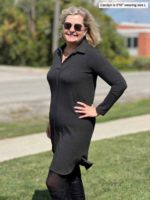 Woman smiling and standing outside while wearing Miik's Finian shirt collar long sleeve dress in charcoal, boots and sunglasses