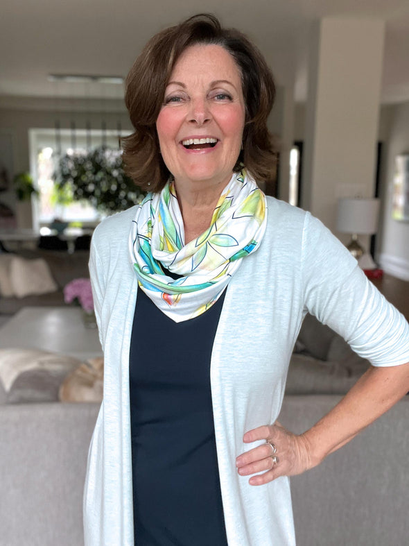 Woman smiling wearing Miik's Flora infinity scarf in tropical leaf, along with a light blue cardigan and navy top