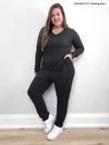 Woman standing in front of a white wall with her hand in the pocket wearing Miik's Fraya stretchy lounge jumpsuit in charcoal