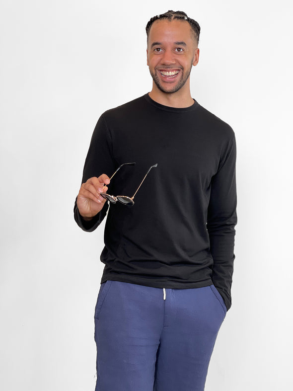 Man standing in front of a wall earring Miik's Jamie round neck long-sleeve in black with blue sweatpants.