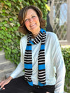 Woman sitting in front of a window smiling while wearing Miik's halona tie scarf in blue black and white stripe with the kallyn top.