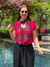 Woman standing in front of a pool wearing Miik's halona scarf in pink and black stripe along with a pink sutton v-neck classic tea and the faye wide leg capri pants in black
