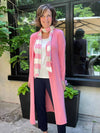 Woman standing in front of a window smiling while wearing Miik's halona tie scarf in pink and white stripe with the robin cardigan in pink.