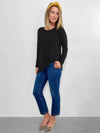 Woman standing in front of a wall wearing Miik's Harmony twisted hem top in black with jeans.